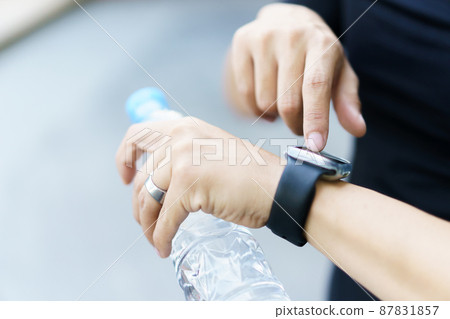 Active Asian young sportsman using a smartwatch or smart fitness band to track his outdoor workout and activities, man reviewing an exercise and health information after finished outdoor workout. Active Asian young sportsman using a smartwatch or smart fitness band to track his outdoor workout and activities, man reviewing an exercise and health information after finished outdoor workout. 87831857