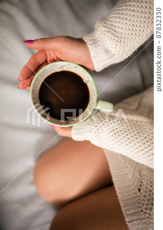 Neat female legs on sofa. Close-up view of a cup of coffee while relaxing. Neat female legs on sofa. Close-up view of a cup of coffee while relaxing. 87832350
