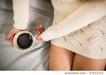 Neat female legs on sofa. Close-up view of a cup of coffee while relaxing. Neat female legs on sofa. Close-up view of a cup of coffee while relaxing. 87832352