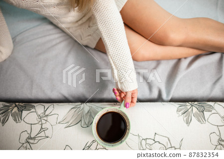 Sexy legs of shapely girl. She is holding a cup of hot coffee. 87832354