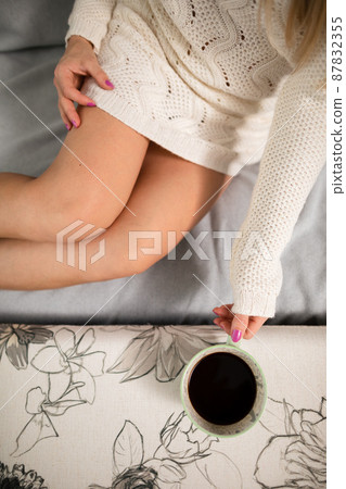 The slim legs of a shapely girl. She is holding a cup of hot coffee. 87832355