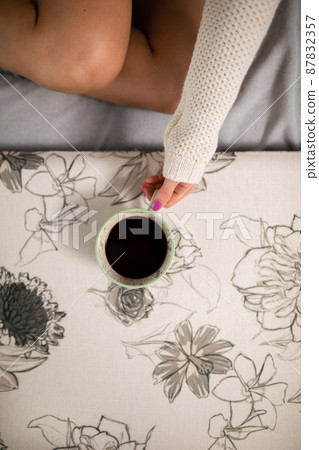 The slim legs of a shapely girl. She is holding a cup of hot coffee. 87832357