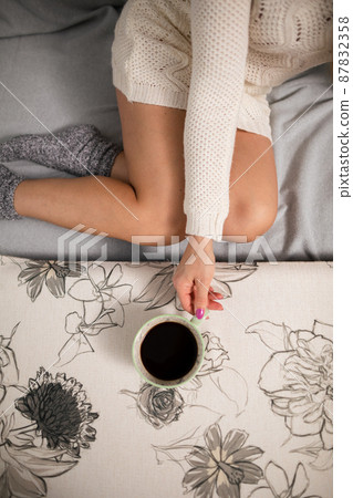Sexy legs of shapely girl. She is holding a cup of hot coffee. 87832358