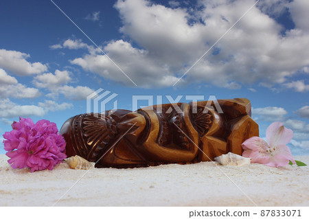 Antique Wooden Mask From Hawaii on Beach With Flowers and Blue Sky Antique Wooden Mask From Hawaii on Beach With Flowers and Blue Sky 87833071