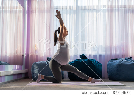 Beautiful young pregnant woman is engaged in pilates. The expectant mother plays sports while waiting for the birth of a child. 87834624