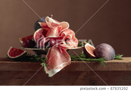 Prosciutto with figs, rosemary, and red olives. 87835202