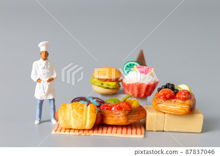 Miniature Baker standing with Sweet dessert on grey background. Miniature Baker standing with Sweet dessert on grey background. 87837046