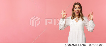 Portrait of happy and pleased good-looking blond woman in white dress, recommend great product, leave positive review, show okay signs and smiling satisfied, standing pink background 87838388