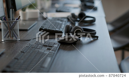 Call center desk with audio headsets and computers, technology used for sutomer care service job. Telemarketing concept at telework office with headphones and monitors. Close up. 87840724