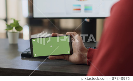 Businessman using horizontal green screen on smartphone, looking at isolated mockup copyspace with blank chroma key background. Office employee working with template on mobile phone. Close up. 87840975