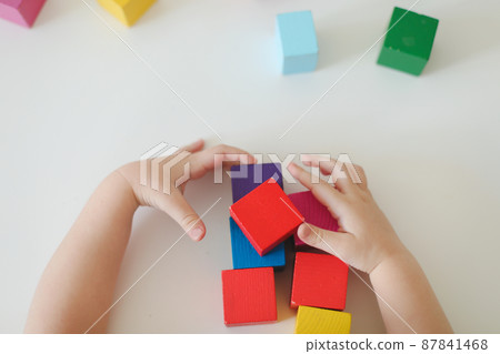 Top view on child hands playing and building with colorful wooden toy bricks on white wooden table. Early learning and development 87841468