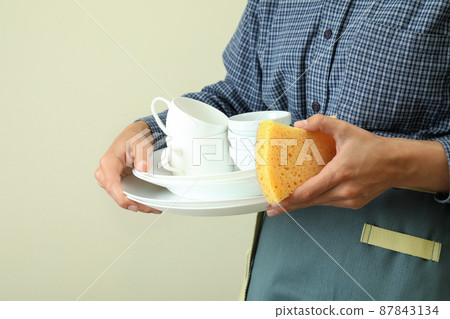 Woman in apron holds clean dishware, close up 87843134