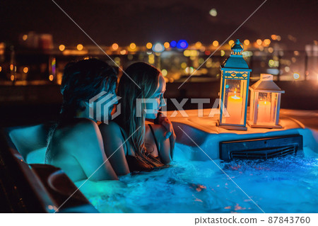 Portrait of young carefree happy smiling couple relaxing at hot tub during enjoying happy traveling moment vacation life against the background of green big mountains at night Portrait of young carefree happy smiling couple relaxing at hot tub during enjoying happy traveling moment vacation life against the background of green big mountains at night 87843760