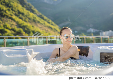 Portrait of young carefree happy smiling woman relaxing at hot tub during enjoying happy traveling moment vacation life against the background of green big mountains 87843829