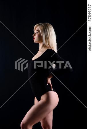 Young blonde plump woman with bright makeup in black bodysuit at dark background 87844937