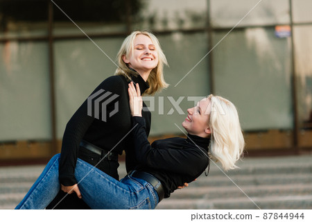 Two young females walking smiling embracing and kissing outdoor in the city 87844944
