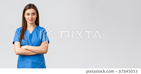Healthcare workers, prevent virus, insurance and medicine concept. Confident smiling female nurse, doctor in blue scrubs, cross arms chest and look determined. Fighting covid-19 outbreak, stay home 87845033