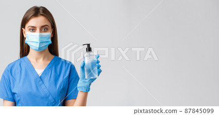 Covid-19, preventing virus, healthcare workers concept. Young pretty professional doctor, female nurse in medical mask and scrubs, showing hand sanitizer or soap to protect from coronavirus Covid-19, preventing virus, healthcare workers concept. Young pretty professional doctor, female nurse in medical mask and scrubs, showing hand sanitizer or soap to protect from coronavirus 87845099