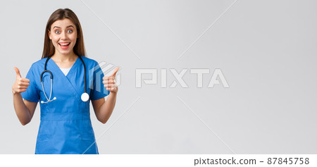Medical workers, healthcare, covid-19 and vaccination concept. Enthusiastic and upbeat female nurse, doctor in blue scrubs, think wonderful idea, show thumbs-up in approval Medical workers, healthcare, covid-19 and vaccination concept. Enthusiastic and upbeat female nurse, doctor in blue scrubs, think wonderful idea, show thumbs-up in approval 87845758