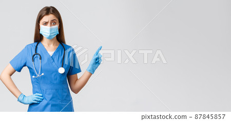 Covid-19, preventing virus, health, healthcare workers and quarantine concept. Skeptical and displeased female nurse or doctor in blue scrubs, medical mask, pointing finger right, frowning doubtful Covid-19, preventing virus, health, healthcare workers and quarantine concept. Skeptical and displeased female nurse or doctor in blue scrubs, medical mask, pointing finger right, frowning doubtful 87845857