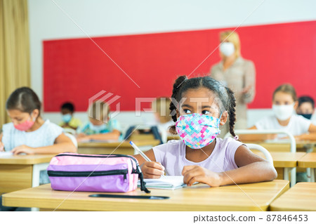 African tween girl in protective mask studying with classmates in school African tween girl in protective mask studying with classmates in school 87846453