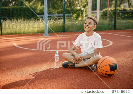 Multiracial boy sitting on a basketball court with a bottle of water 87846653
