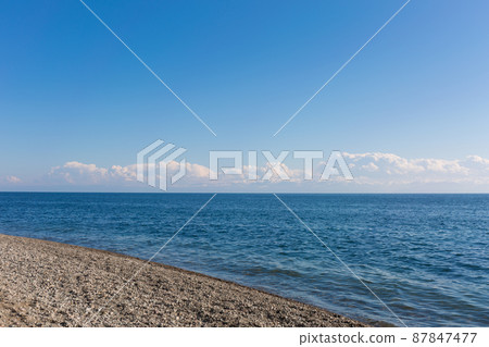 Blue calm sea and white clouds. Snow capped mountains on the horizon. 87847477
