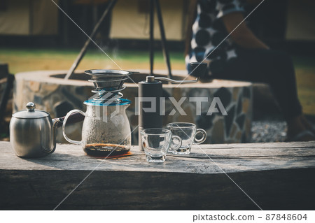 Coffee maker is placed on top of wooden chair in camping area. 87848604