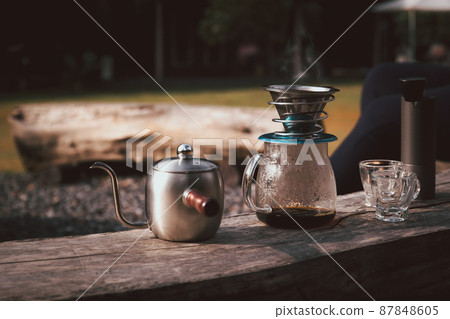 Coffee maker is placed on top of wooden chair in camping area. 87848605