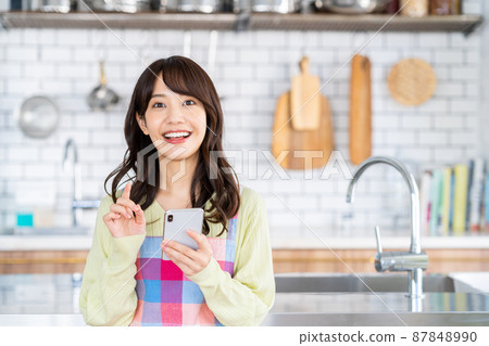 Young woman looking at her smartphone in the kitchen 87848990