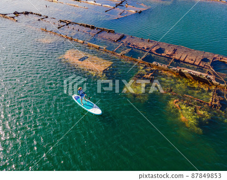 Woman on paddle board, sup next to Abandoned broken shipwreck sticking out of the sea Woman on paddle board, sup next to Abandoned broken shipwreck sticking out of the sea 87849853