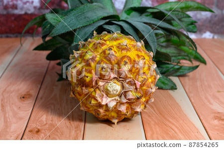 one whole pineapple lies on light boards against the background of a brick wall one whole pineapple lies on light boards against the background of a brick wall 87854265