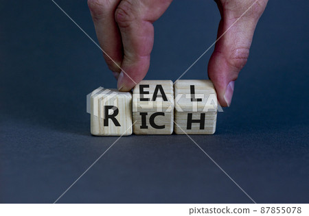 Real rich symbol. Businessman turns wooden cubes with words 'Real rich'. Beautiful grey background. Real rich and business concept. Copy space. Real rich symbol. Businessman turns wooden cubes with words 'Real rich'. Beautiful grey background. Real rich and business concept. Copy space. 87855078