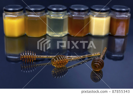 Hexagonal jars with different types and colors of fresh flower honey and a honey spoon Hexagonal jars with different types and colors of fresh flower honey and a honey spoon 87855343