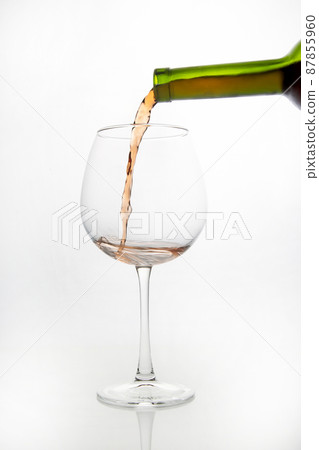 red wine from a bottle is poured into a glass on a light background. 87855960