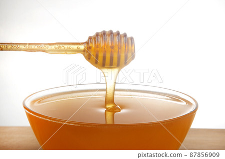 fresh honey dripping from a spoon into a transparent plate on a white background. 87856909