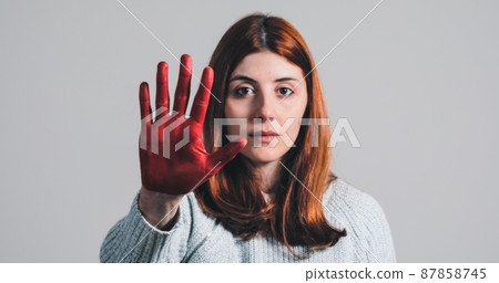 Sad girl raises her hand painted red to stop and protest against violence Sad girl raises her hand painted red to stop and protest against violence 87858745