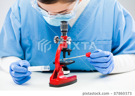 Medical worker UK lab technician microscope examining Coronavirus patient swab test tube sample specimen 87860373