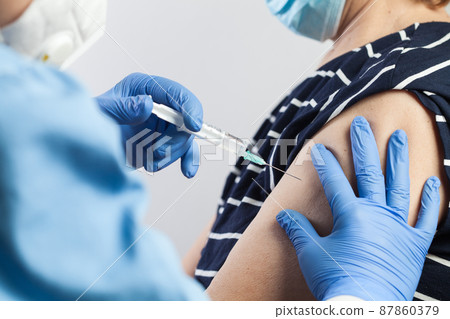 Nurse giving COVID-19 vaccine shot to elderly volunteer patient 87860379