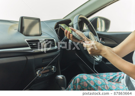 Woman driver charging her smart phone in the car. Woman driver charging her smart phone in the car. 87863664