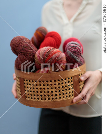 The women's hands hold a wicker basket with skeins of homemade yarn. Vertical frame, selective focus The women's hands hold a wicker basket with skeins of homemade yarn. Vertical frame, selective focus 87866616