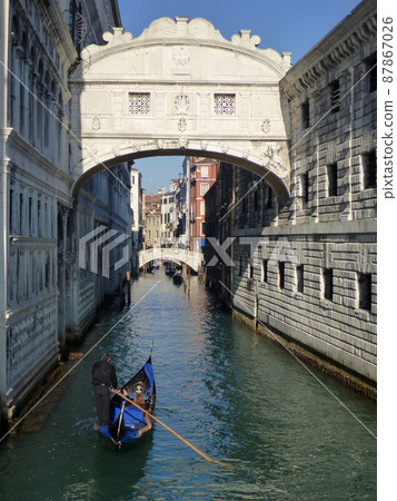 A gondola passing under a narrow canal and a sigh bridge in Venice, Italy 87867026