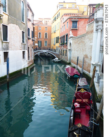 Narrow waterways and a black unmanned gondola for two in Venice, Italy Narrow waterways and a black unmanned gondola for two in Venice, Italy 87867043