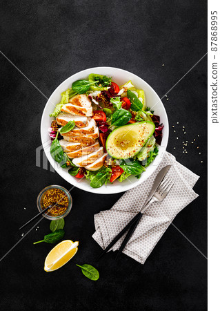 Grilled chicken breast and fresh vegetable salad of tomato, avocado, lettuce and spinach. Top view, flat lay 87868995