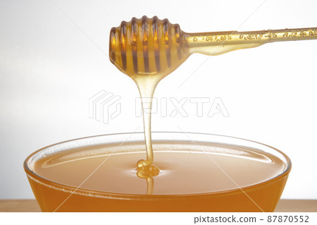 fresh honey dripping from a spoon into a transparent plate on a white background fresh honey dripping from a spoon into a transparent plate on a white background 87870552