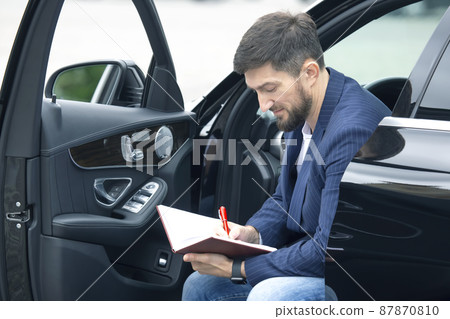 Successful businessman is engaged with documents while sitting near his prestigious car Successful businessman is engaged with documents while sitting near his prestigious car 87870810
