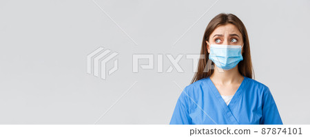 Covid-19, preventing virus, health, healthcare workers and quarantine concept. Skeptical distressed female nurse or doctor in blue scrubs, medical mask, look upper left corner uncertain or puzzled 87874101