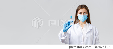 Covid-19, preventing virus, healthcare workers and quarantine concept. Determined professional doctor in medical mask and rubber gloves, showing syringe filled with coronavirus vaccine Covid-19, preventing virus, healthcare workers and quarantine concept. Determined professional doctor in medical mask and rubber gloves, showing syringe filled with coronavirus vaccine 87874122