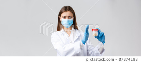 Covid-19, preventing virus, healthcare workers and quarantine concept. Concerned and displeased doctor in medical mask, gloves, reject, disapprove using medicine, showing bad pills Covid-19, preventing virus, healthcare workers and quarantine concept. Concerned and displeased doctor in medical mask, gloves, reject, disapprove using medicine, showing bad pills 87874188