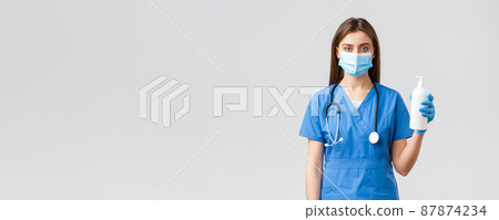 Covid-19, preventing virus, health, healthcare workers and quarantine concept. Professional female nurse in clinic, doctor wearing medical mask, scrubs, holding hand sanitizer or soap 87874234